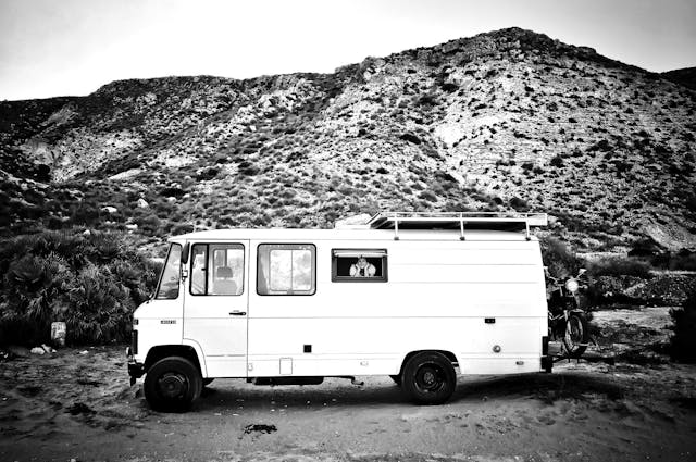 woman smiling out of campervan window parked infront of a hill